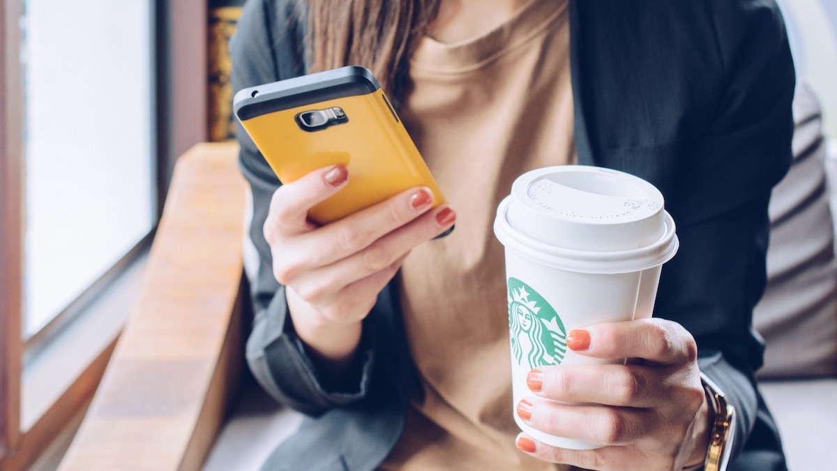 woman holding a cell phone in one hand and a grande starbucks beverage in the order