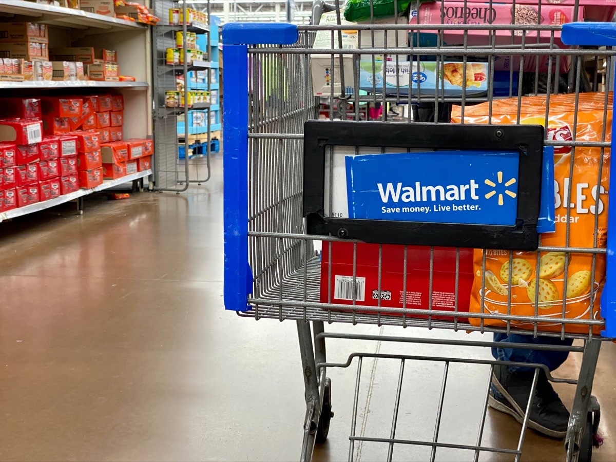 closeup of Walmart shopping cart in the middle of an isle with some items already inside.