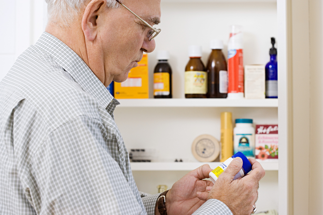 A senior man looking at bottles of medicine and medication in his medicine cabinet