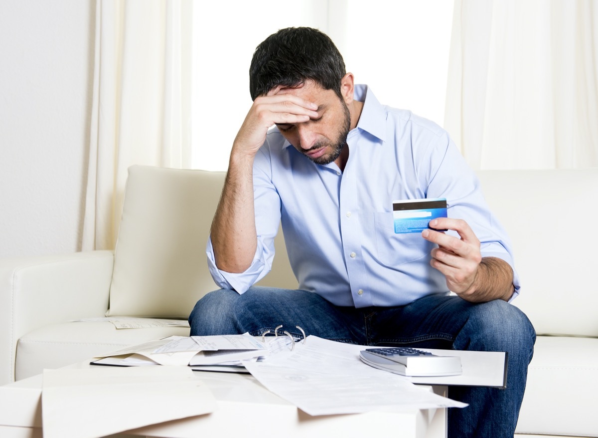 Latin-American man looking down at bills and holding a credit card while looking stressed