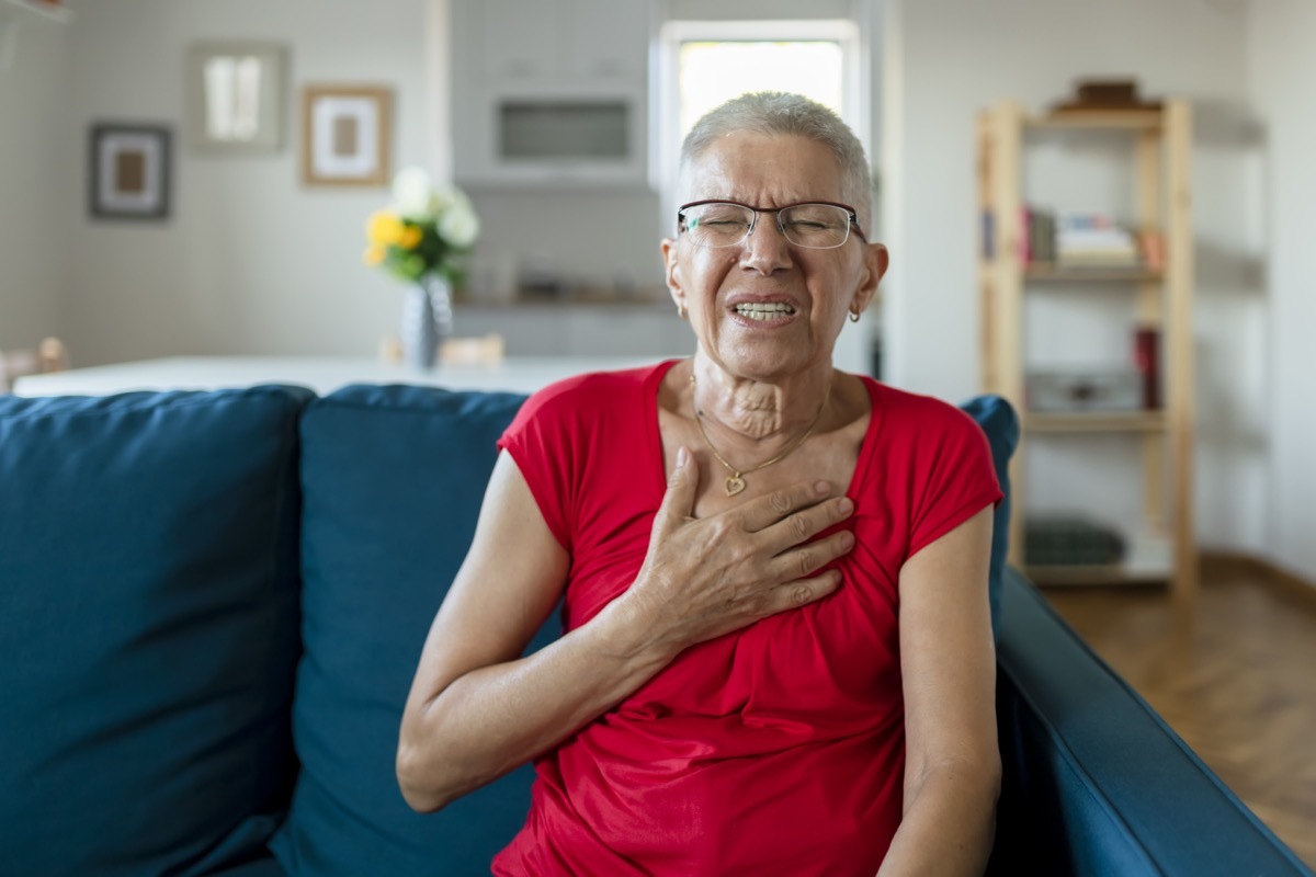 Senior Woman Suffering From Chest Pain While Sitting on Sofa at Home. Old Age, Health Problem, Vision and People Concept. Heart Attack Concept. Elderly Woman Suffering From Chest Pain Indoor