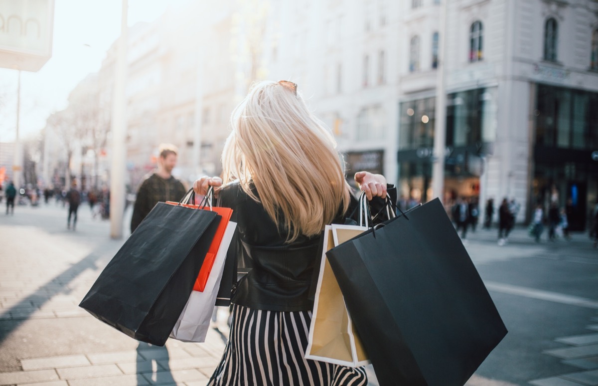 girl walking from store with a lot of shopping bags with back turned to camera