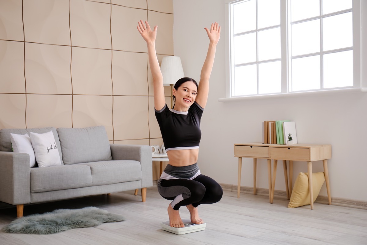 Happy young woman measuring her weight at home