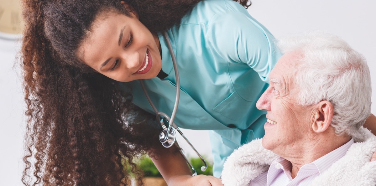 nurse with a stethoscope covering an elderly man with a blanket in a nursing home