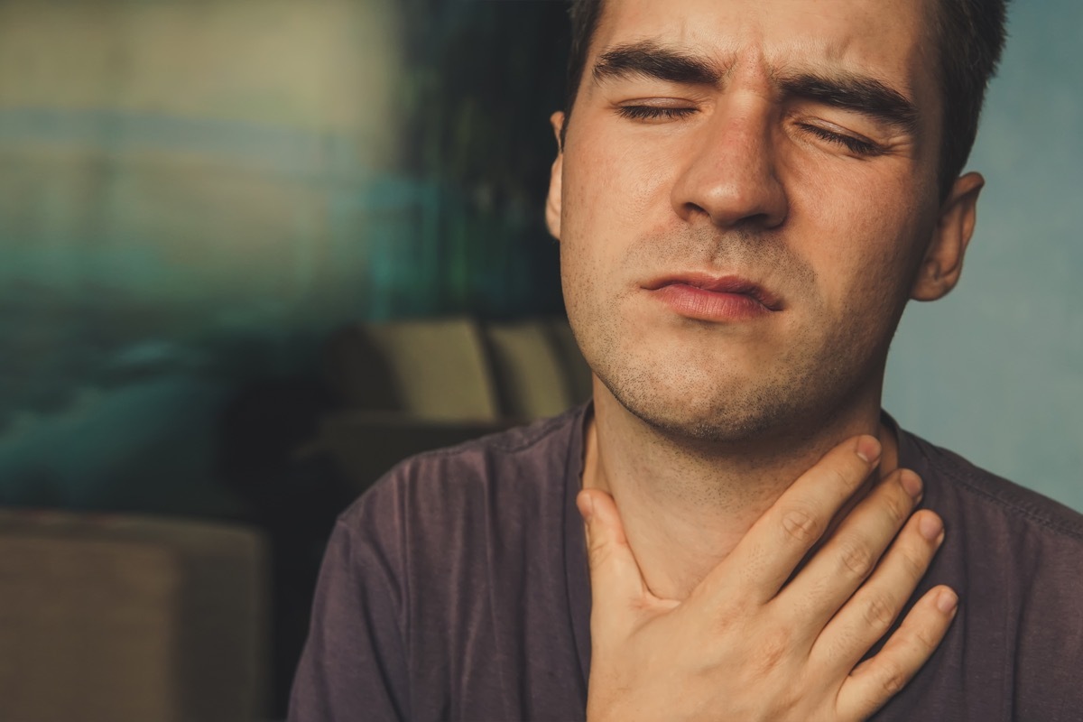 people, healthcare and problem concept. unhappy man touching his neck and suffering from throat pain while sitting on couch at home.