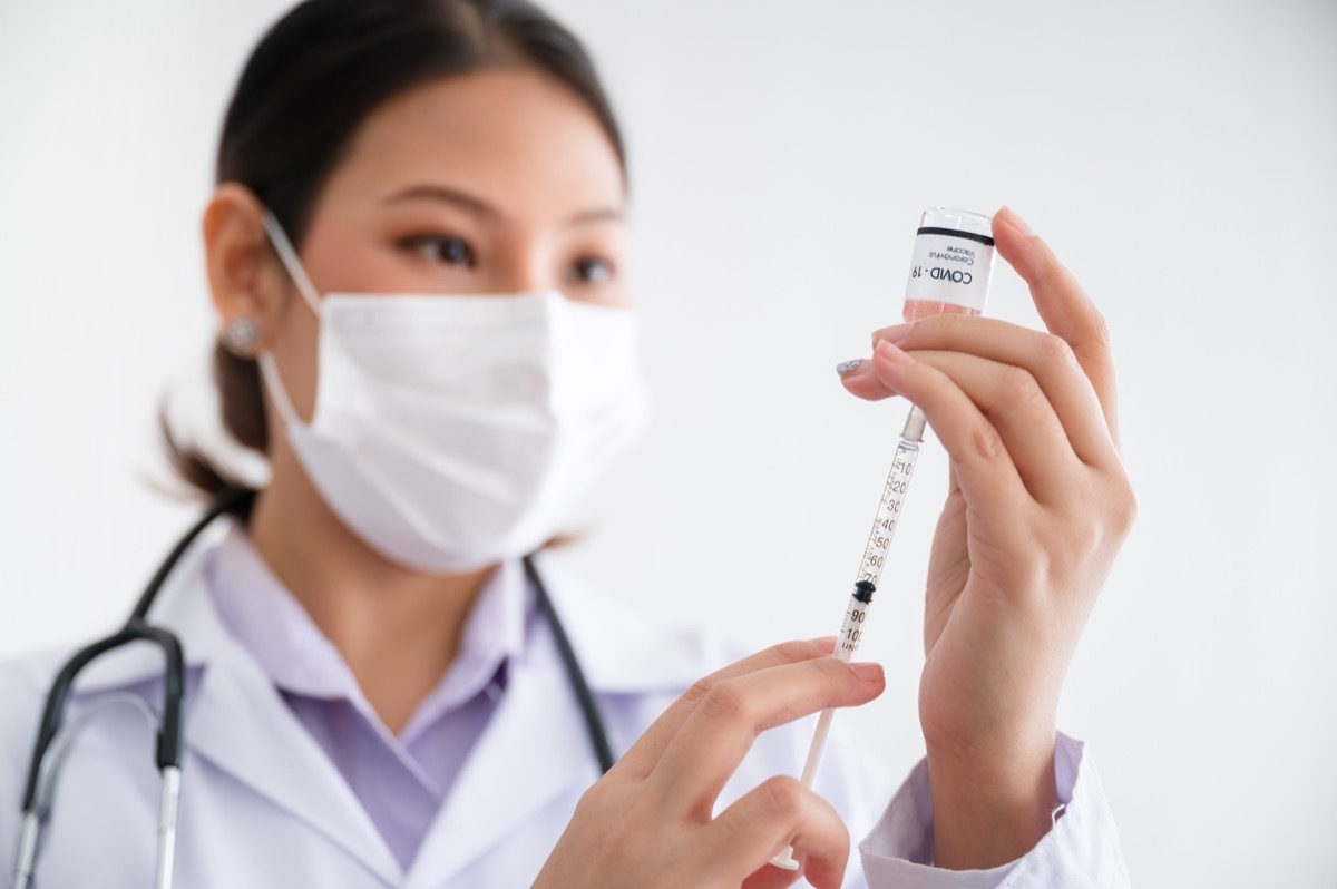 Female doctor wearing a mask stands holds a syringe with a bottle of vaccine for protection Coronavirus19 in a laboratory. Concept of preventing the spread of COVID-19.