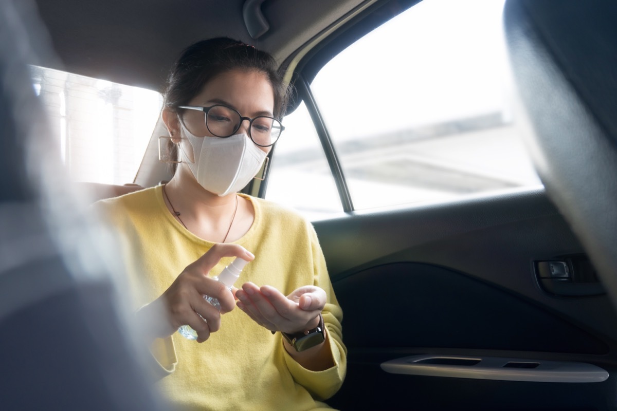 Female Passenger in green or yellow shirt and protective mask spraying disinfectant alcohol on her palms and her hands for prevent coronavirus or Coronavirus while her in a car. Cleaning, Antiseptic, Hygiene, Healthy and Health care concept.