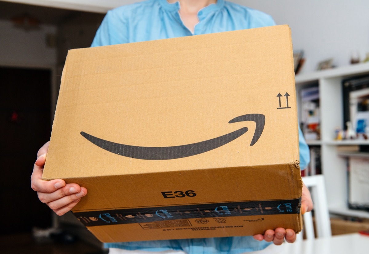 PARIS, FRANCE - JUL 4, 2018: Woman receiving Amazon Prime package delivered preparing to do the unboxing, proud Amazon Prime client with library in background