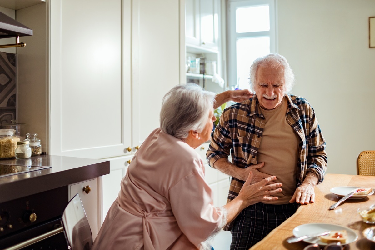 Close up of a senior man experiencing stomach pain while having breakfast with his wife