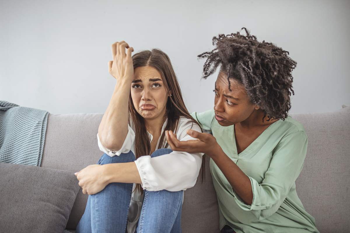 Young lady sharing her problem with friend. female in depression. Woman omforting hes sad friend sitting on a couch in the living room at home