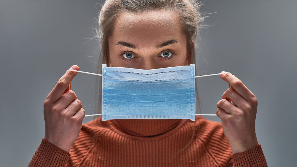 A woman holding a protective face mask over her mouth about to put it on.