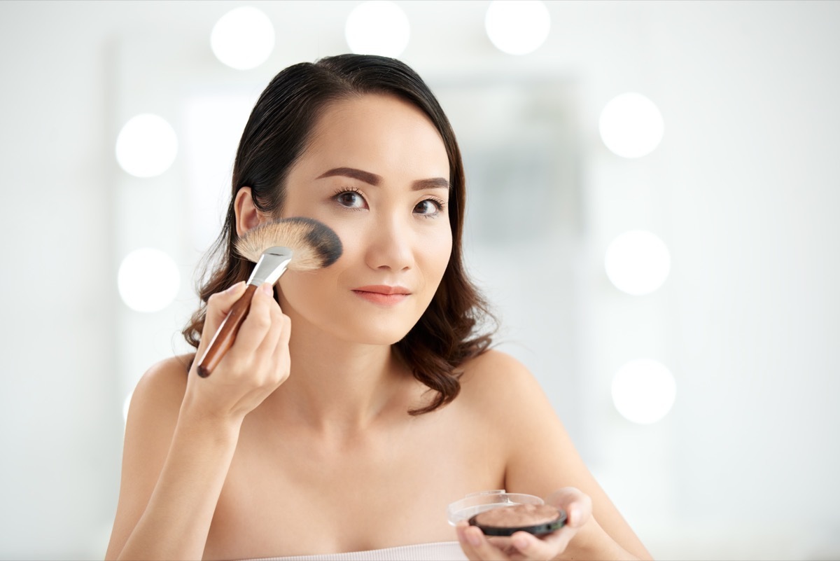 woman applying makeup and highlighter on highest points of her cheeks 