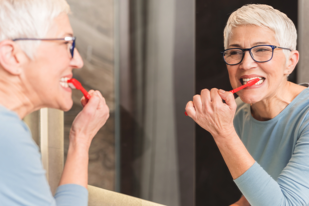 A senior woman brushing her teeth in the mirror