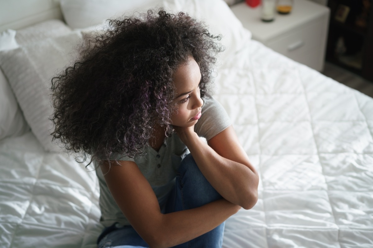 Lonely young latina woman sitting on bed. Depressed hispanic girl at home, looking away with sad expression