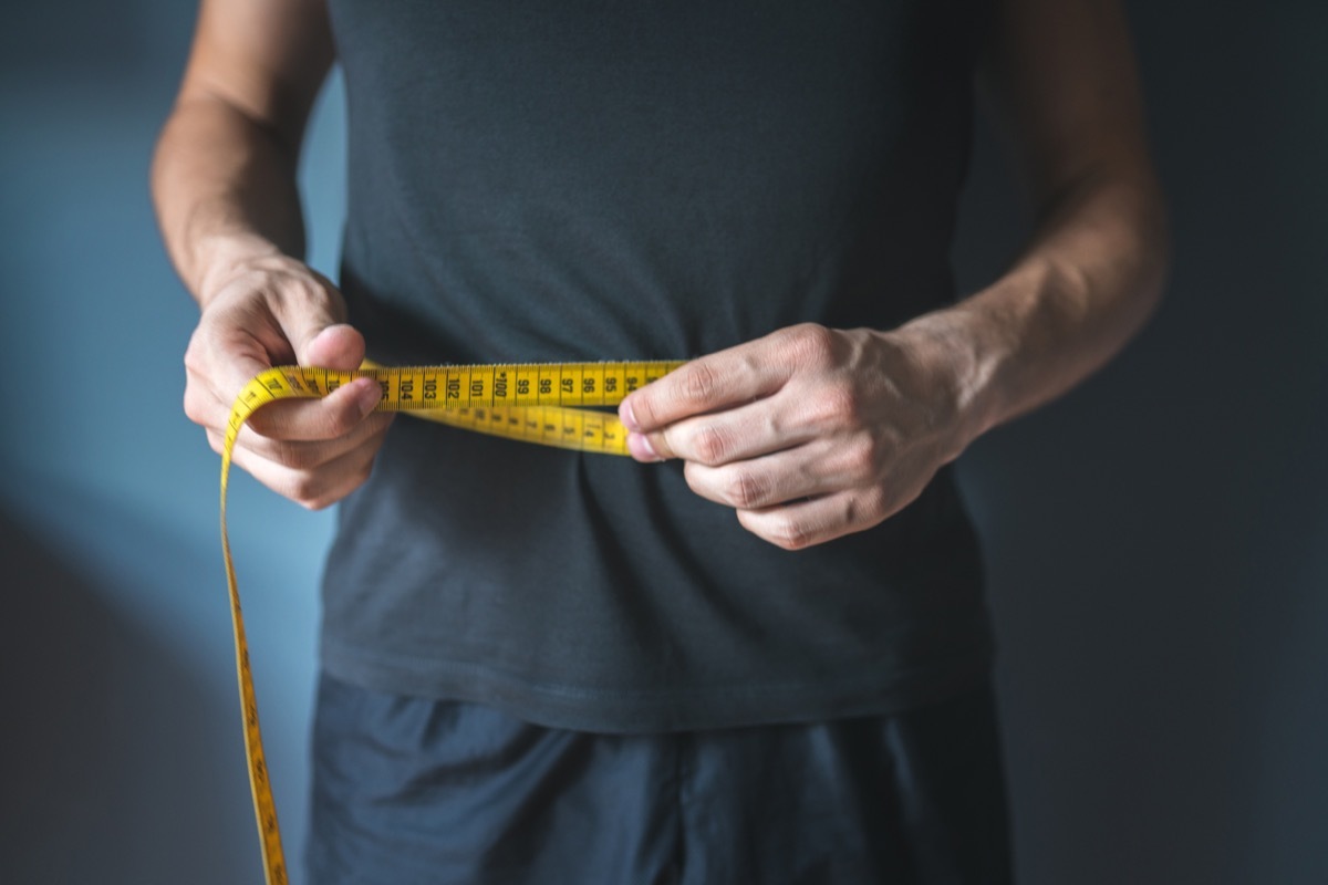 man measures his waist, checking for weight loss