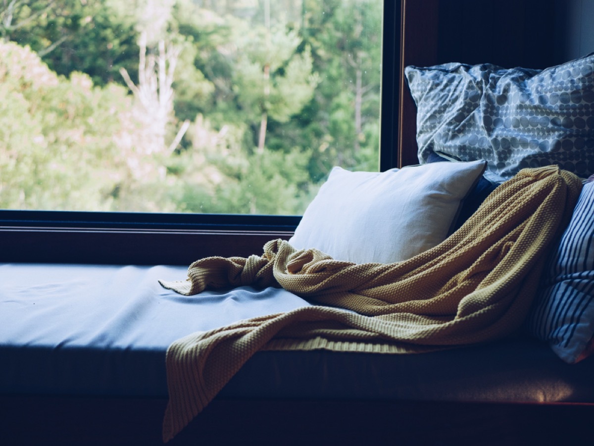 reading nook with two blue pillows, yellow throw, and white pillow in front of window