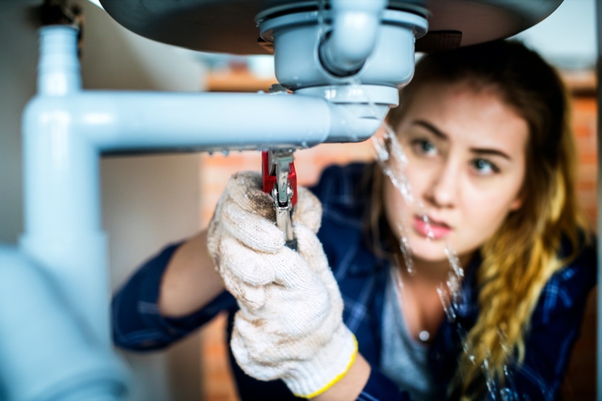 young white woman fixing leaking pipe