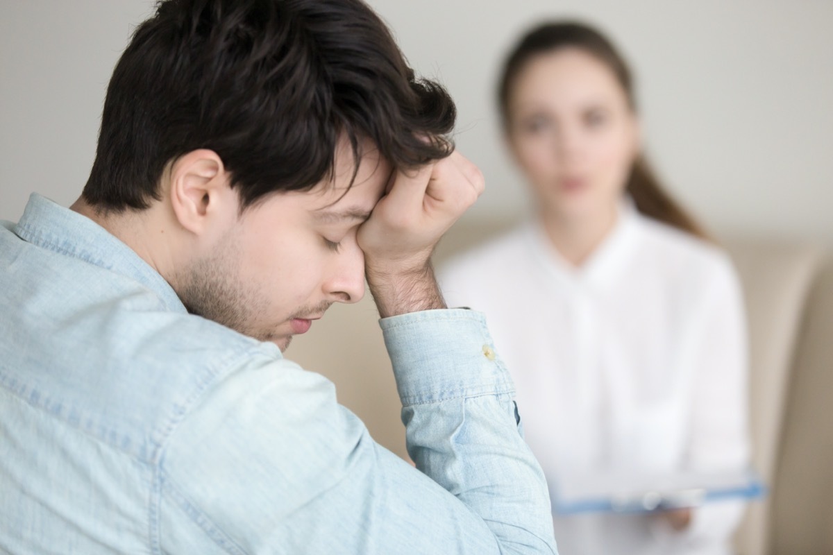 guy touching his forehead, having a headache or migraine, overworked businessman feeling tired, stressed and exhausted, female doctor, nurse or colleague standing in the background