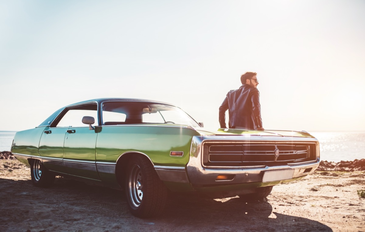 Bearded man leaning against green vintage car on the beach