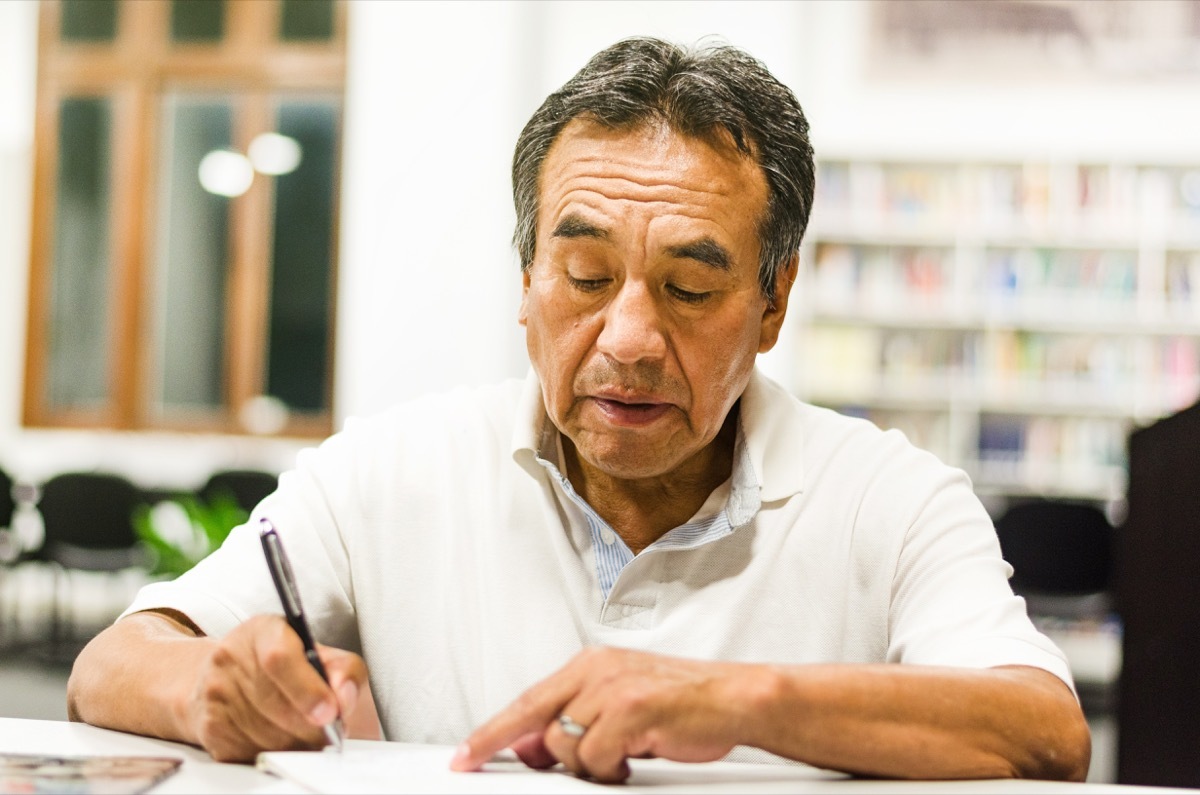 serious senior man sitting on a library bench writing in his book. Senior man sitting in a university classroom.