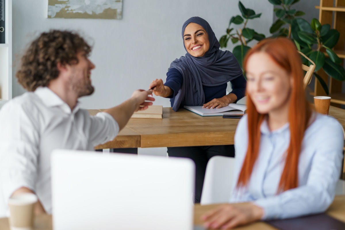 woman in hijab lending white male coworker a pen