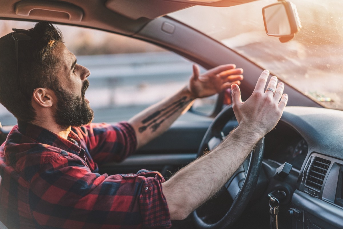 Side view image of irritated man shouting at other drivers while driving on the highway