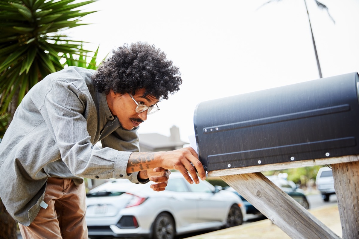 man standing outside and bending over to check for letters in his mailbox