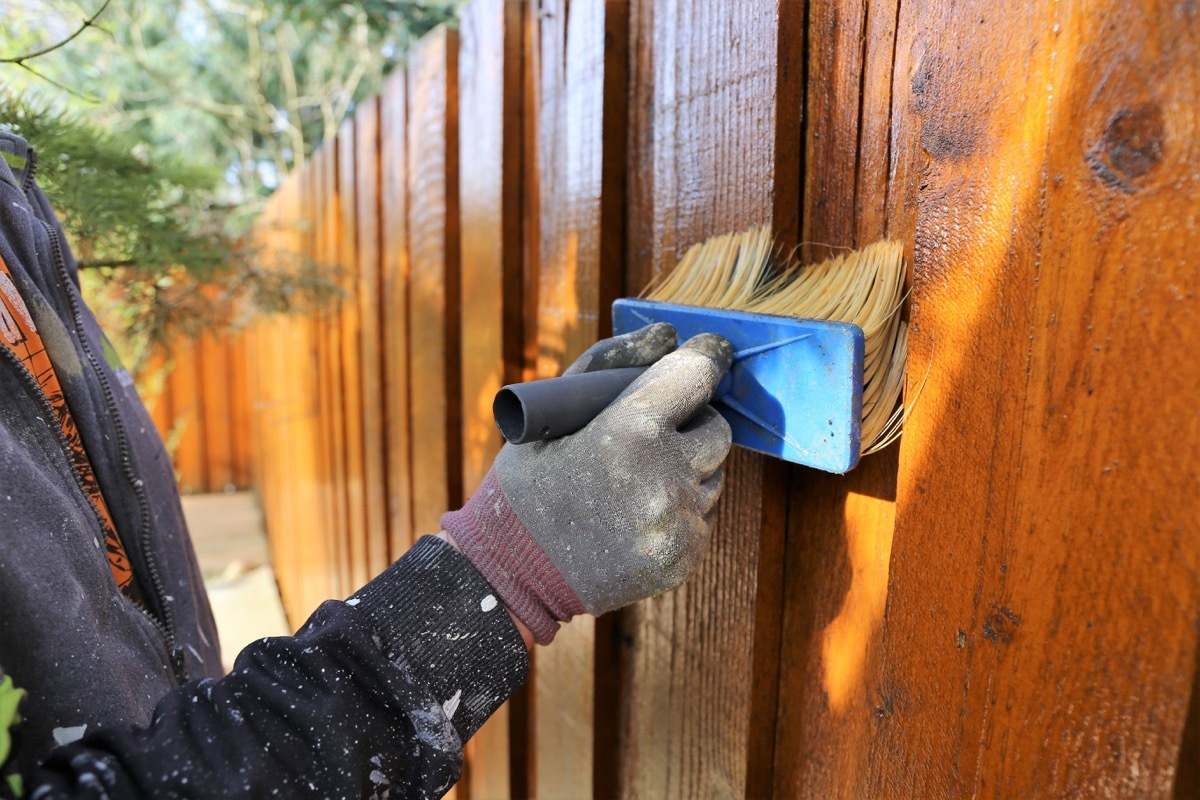 someone painting an outisde fence